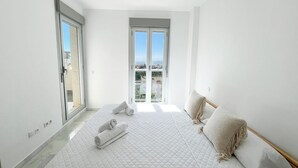 Quarto com cama grande, porta de correr de vidro e vista para a cidade.