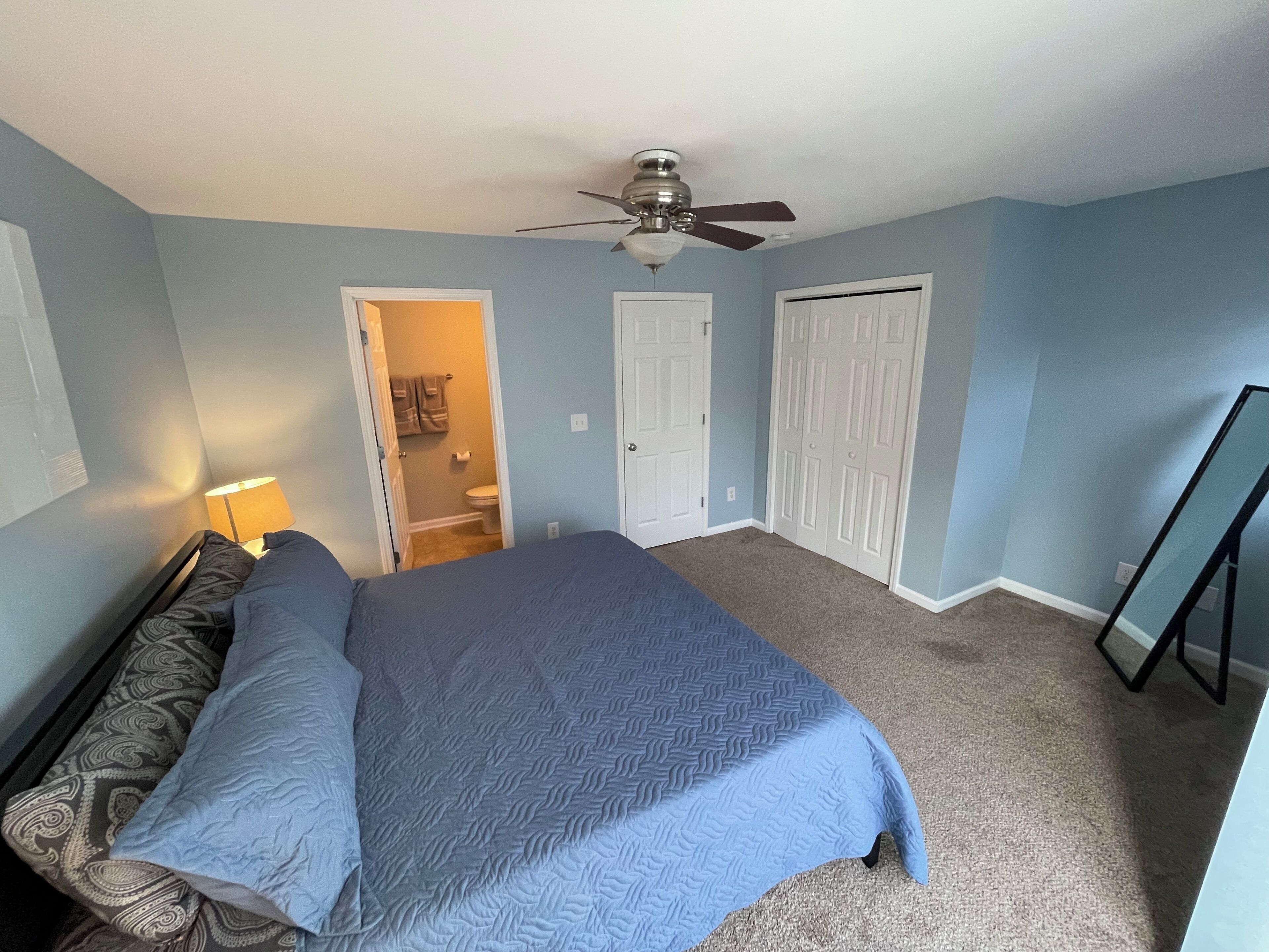 Une chambre à coucher avec un lit, un ventilateur de plafond et une porte donnant sur une salle de bain.