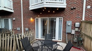 Eine Terrasse mit einem runden Tisch und Stühlen, einem Holzzaun und einem Backsteinhaus mit Balkon.