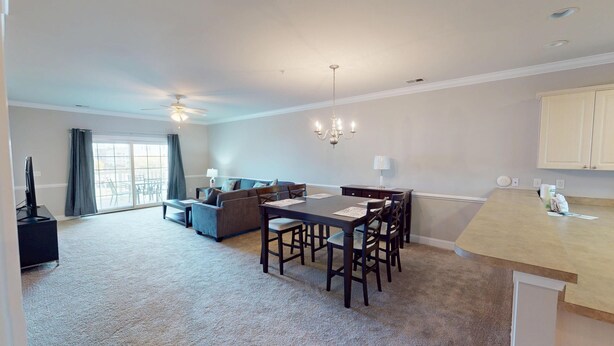 A modern living room with a sofa, dining table, and chairs. There is a ceiling fan, a chandelier, and a television.