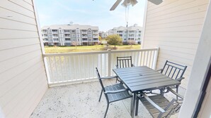 A balcony with a table and chairs, overlooking a residential area with multi-story buildings.