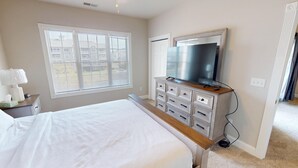 A bedroom with a bed, a dresser, a television, and a window with blinds.