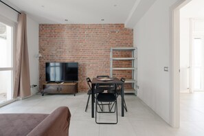 A living room with a brick wall, a TV, a dining table with chairs, and a sofa.