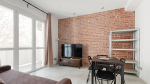 Un salon moderne avec un mur en briques, un téléviseur à écran plat, une table à manger avec des chaises et un canapé.