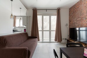 A modern living space with a sofa, a dining table, a TV, and a kitchen area.