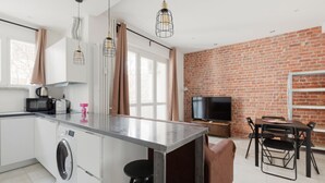 Une cuisine moderne dotée d’un îlot central, d’un coin repas avec un mur en briques et d’un téléviseur à écran plat.