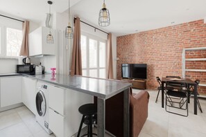 Una cocina moderna con una isla central, un comedor con pared de ladrillo y un televisor de pantalla plana.