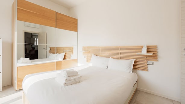 Une chambre d’hôtel moderne dotée d’un grand lit, d’une tête de lit en bois, d’un grand miroir et d’une armoire intégrée.