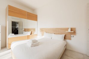 A modern hotel room with a large bed, a wooden headboard, a large mirror, and a built-in wardrobe.