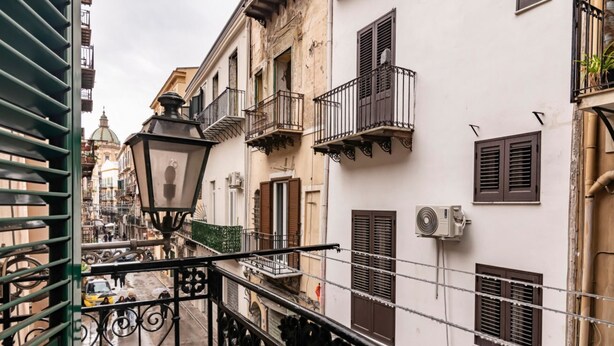 Un vicolo stretto con edifici provvisti di balconi e persiane, un lampione e un condizionatore d'aria.