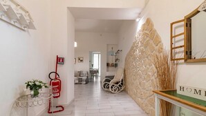 Un corridoio con un estintore, un tavolino con fiori, una sedia e un muro in pietra con uno specchio e un cartello che recita 'HOME'.