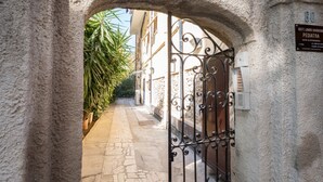 A stone archway leading to a building with a metal gate, a sign indicating a pediatric clinic, and a paved path with plants. - GuestHost - A Step from the Beach - Roomy Apt with Sea Glimpse (Arma di Taggia)