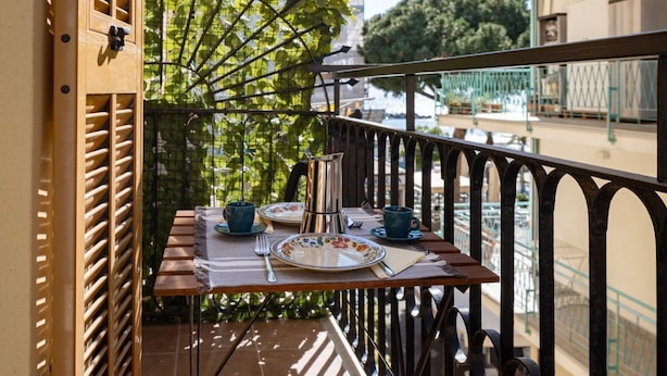 A balcony with a table set for two, a metal kettle, and a view of a building with a balcony railing. - GuestHost - A Step from the Beach - Roomy Apt with Sea Glimpse (Arma di Taggia)
