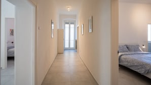 A hallway leading to a bedroom with a bed, framed pictures on the walls, and a door at the end. - GuestHost - A Step from the Beach - Roomy Apt with Sea Glimpse (Arma di Taggia)