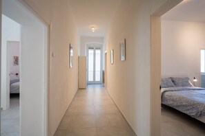 A hallway leading to a bedroom with a bed, framed pictures on the walls, and a door at the end.