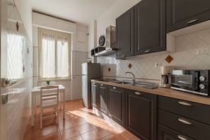 Una cocina con armarios oscuros, encimera blanca, lavabo, estufa y ventana con cortinas.