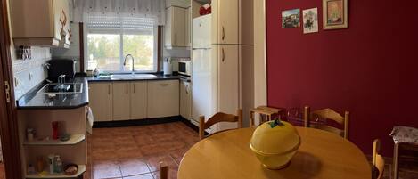 A compact kitchen with a sink, stove, and cabinets. There is a dining table with chairs and a yellow bowl on it.