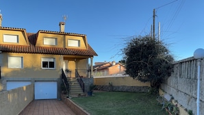 Una propiedad residencial con un camino pavimentado que conduce a una puerta principal, un muro de piedra y un pequeño jardín.