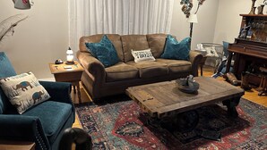 Una sala de estar acogedora con un sofá marrón, cojines color turquesa, una mesa de centro de madera y una alfombra estampada.