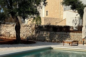 A pool area with a stone wall, a bench, and a tree. - The Olive Reatreat Villa with private pool, sunbeds & garden (Monopoli)