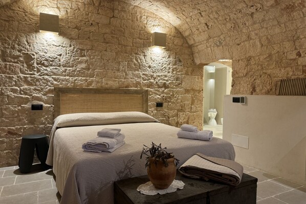 A stone-walled bedroom with a bed, a small table with a plant, and a nightstand.