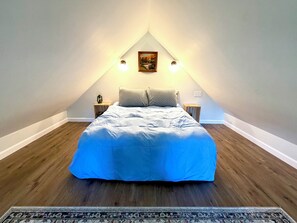 Une chambre à coucher comprenant un lit, deux tables de chevet, une commode, un tableau accroché au mur et un tapis à motifs.