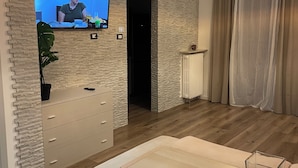 Ein modernes Wohnzimmer mit Fernseher an einer Ziegelwand, einem Holztisch, einer Couch und einer Pendelleuchte.