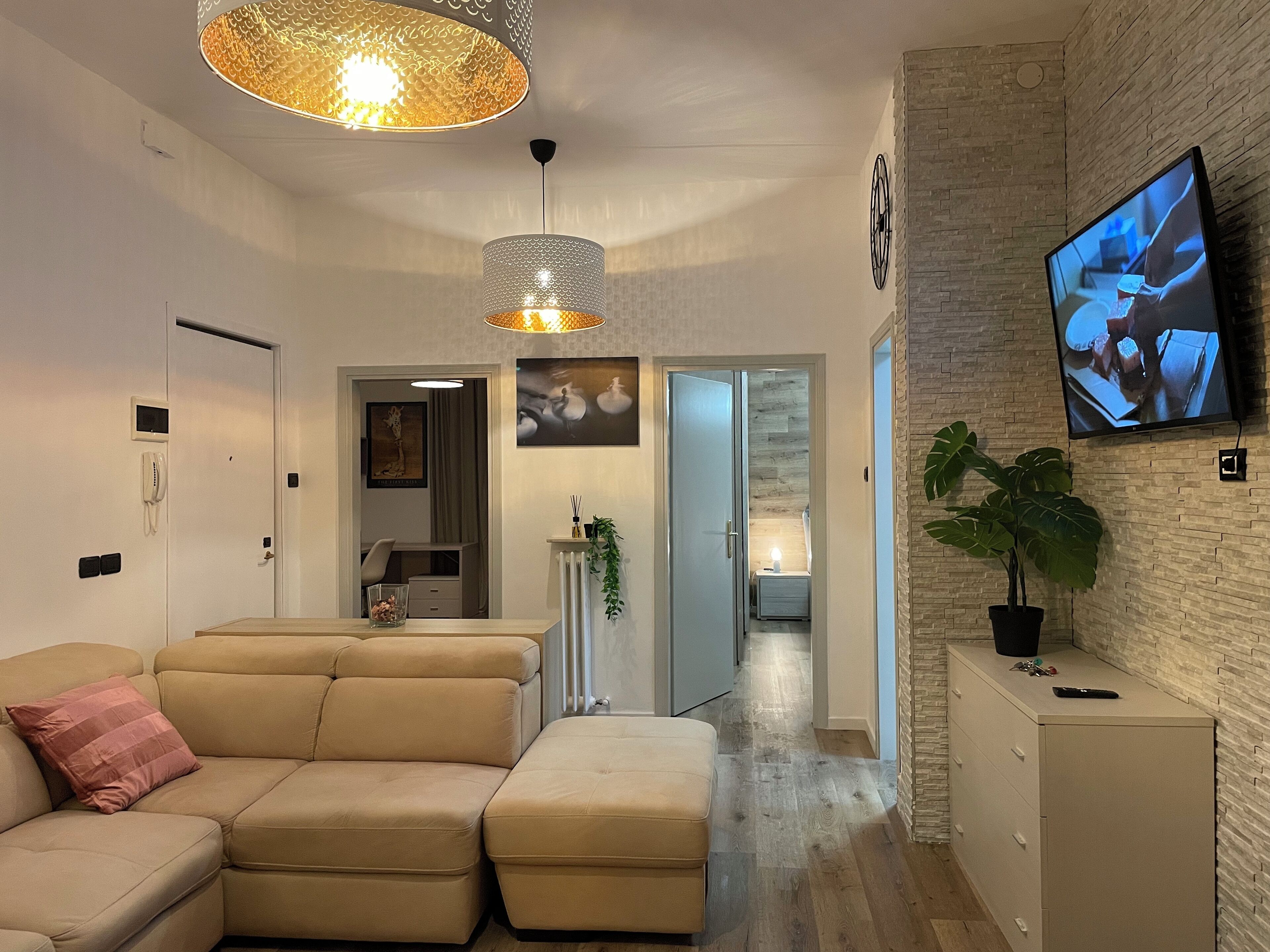 A modern living room with a sectional sofa, a TV mounted on the wall, and a potted plant.