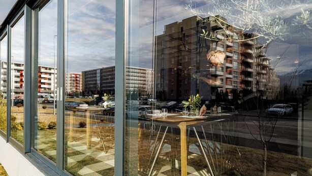 A modern restaurant with large glass windows offering views of urban buildings and a parking area.