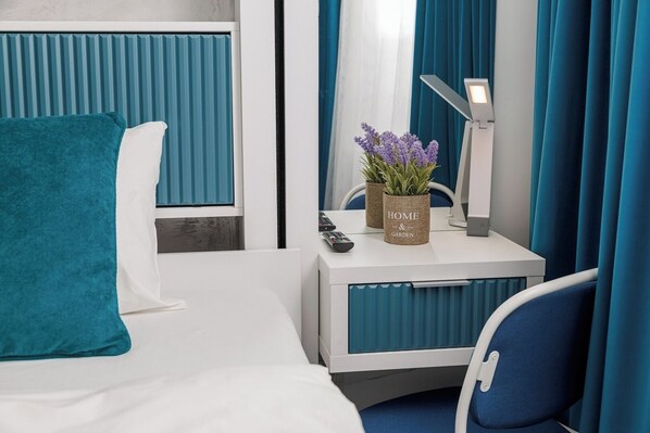 A modern hotel room with a bed, a desk with a lamp, a remote control, and a potted plant.