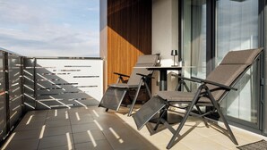 A modern balcony with two lounge chairs, a small table, and a glass door leading to a terrace.