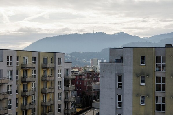 A multi-story residential building with balconies, a view of mountains, and a distant tower.