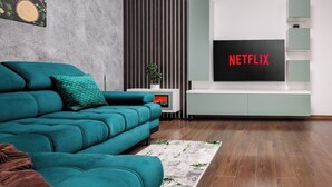 A modern living room with a teal sofa, a flat-screen TV mounted on a wall, and a small side table with a plant.