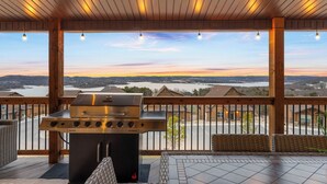 A covered outdoor area with a grill, wicker furniture, and a view of a lake and buildings.