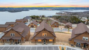 A row of wooden cabins with a view of a lake and distant hills during sunset.