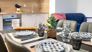 Une cuisine moderne équipée d’un four à micro-ondes, d’un four et d’un évier. On y trouve une table à manger mise avec des assiettes, des verres et un pain. Une plante en pot est posée sur la table, et un canapé bleu se trouve à l’arrière-plan.