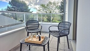 Un balcon avec deux fauteuils en osier noir et un plateau en bois contenant des verres et une théière.