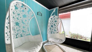 Two white wicker chairs with circular patterns on the backrests, positioned in a room with teal walls and a window overlooking greenery.