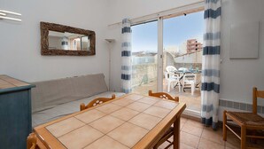 A room with a wooden table, a sofa, a mirror, and a view of a balcony with chairs and a table. - Sunny Terrace & Seaside Charm (Agde)