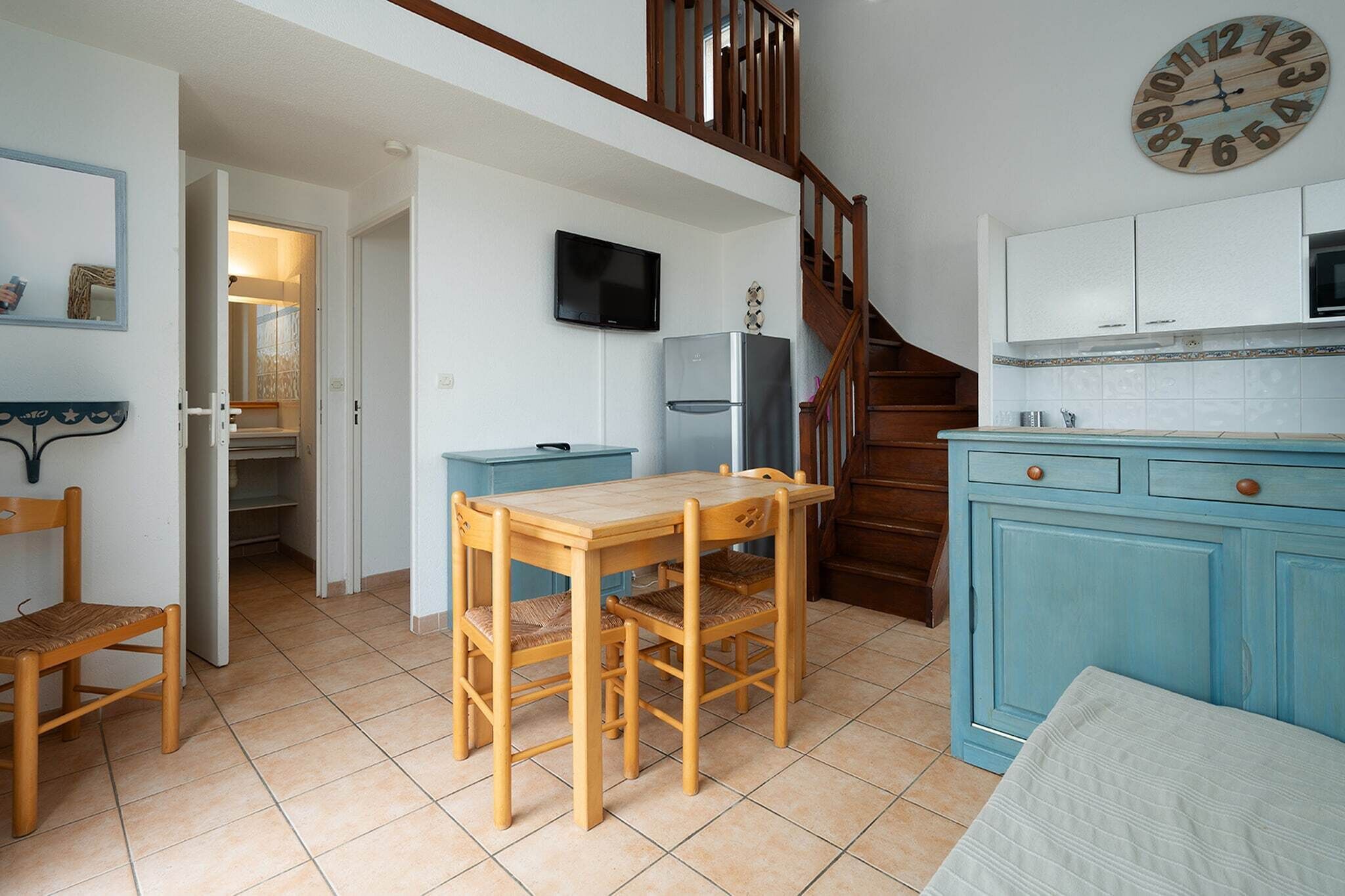 Eine Küche mit einem Holztisch, Stühlen, einem blauen Schrank und einer Uhr an der Wand.