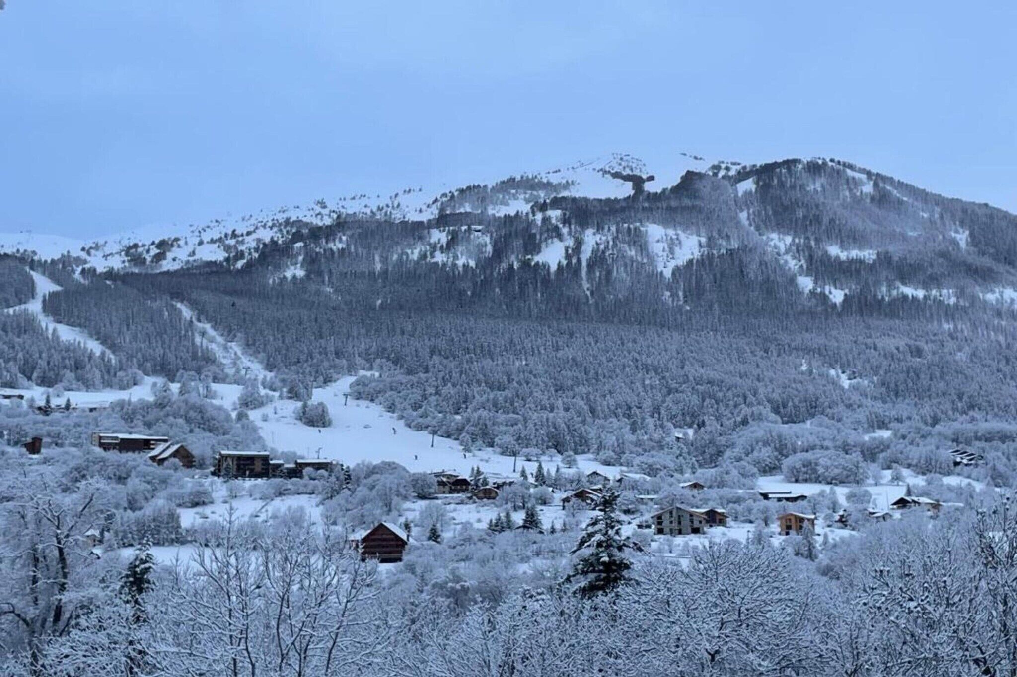 A snow-covered mountain village with wooden houses and a ski slope.