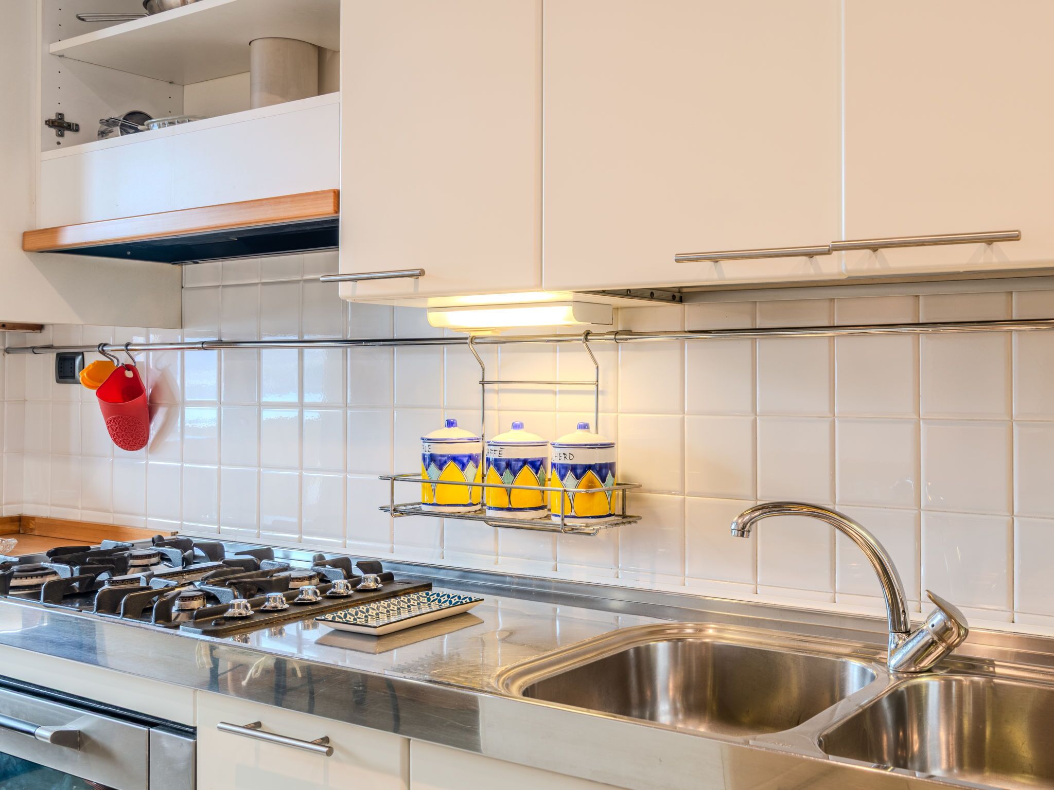 A modern kitchen with a stainless steel sink, a gas stove, and a white tiled backsplash.