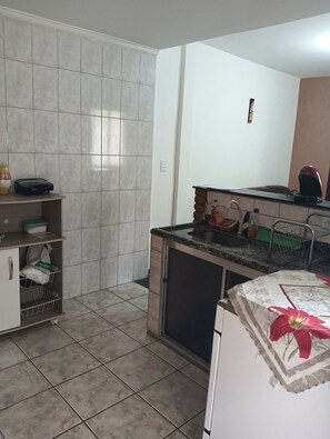 A kitchen with a tiled backsplash, a countertop with a kettle, a sink, and a cabinet with storage baskets.