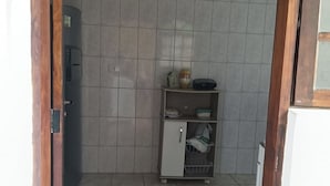 Uma cozinha pequena e azulejada, com geladeira, uma prateleira com utensílios de cozinha e um armário com cesto de arame.