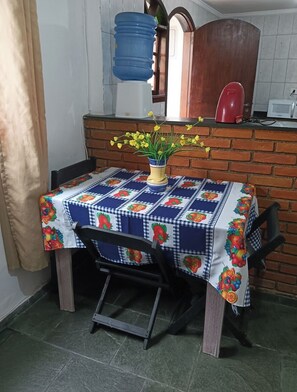 A kitchen area with a table covered in a blue and white checkered tablecloth, a vase with yellow flowers, and a red kettle on the counter.