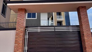 A two-story house with a gated entrance, a balcony on the upper floor, and a clear sky above.