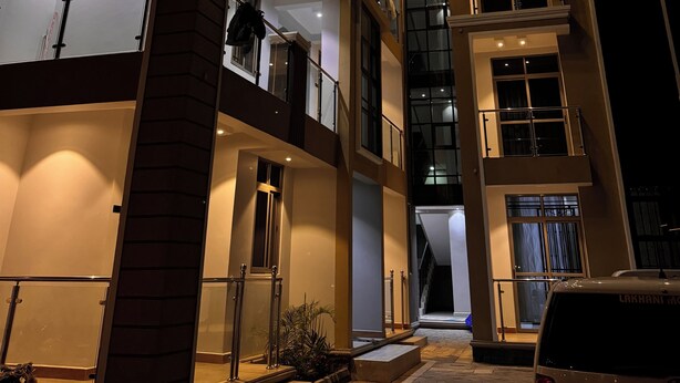A multi-story building with balconies, large windows, and a car parked in front.