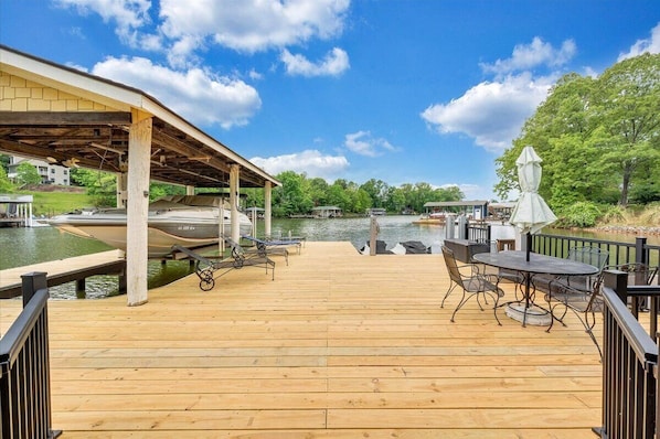 A wooden deck with a covered area, a table with chairs, and a boat docked on the water.