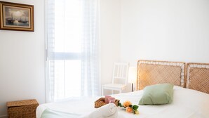 Un lit bien fait, recouvert d’une couverture verte, avec un panier en osier et une serviette enroulée.