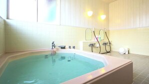 Une salle de bain avec une grande baignoire, une fenêtre et un luminaire fixé au mur.